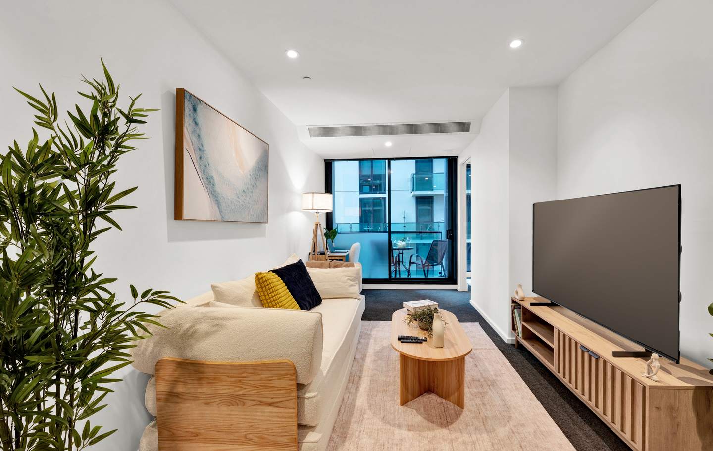 Aurora: living room — a deep sofa facing the 65-inch smart television, with the balcony and the city light beyond