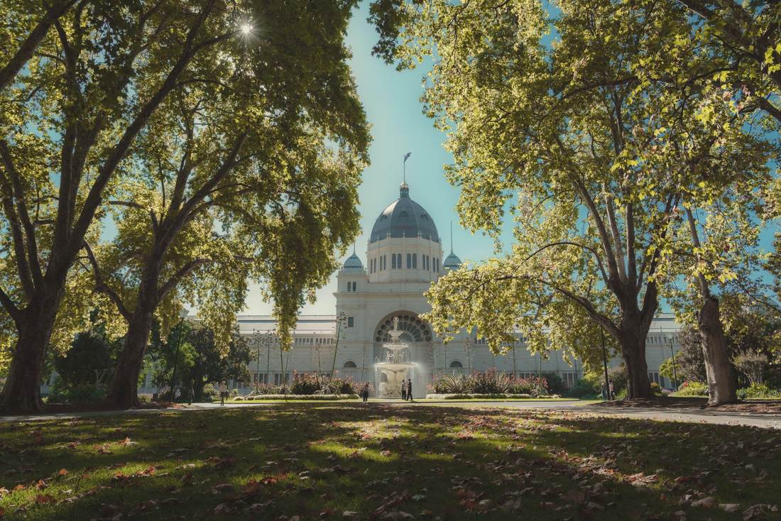 A domed nineteenth-century exhibition hall standing among lawns and tall mature trees under a clear sky.
