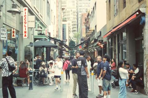 A group gathered in a city laneway lined with cafés.