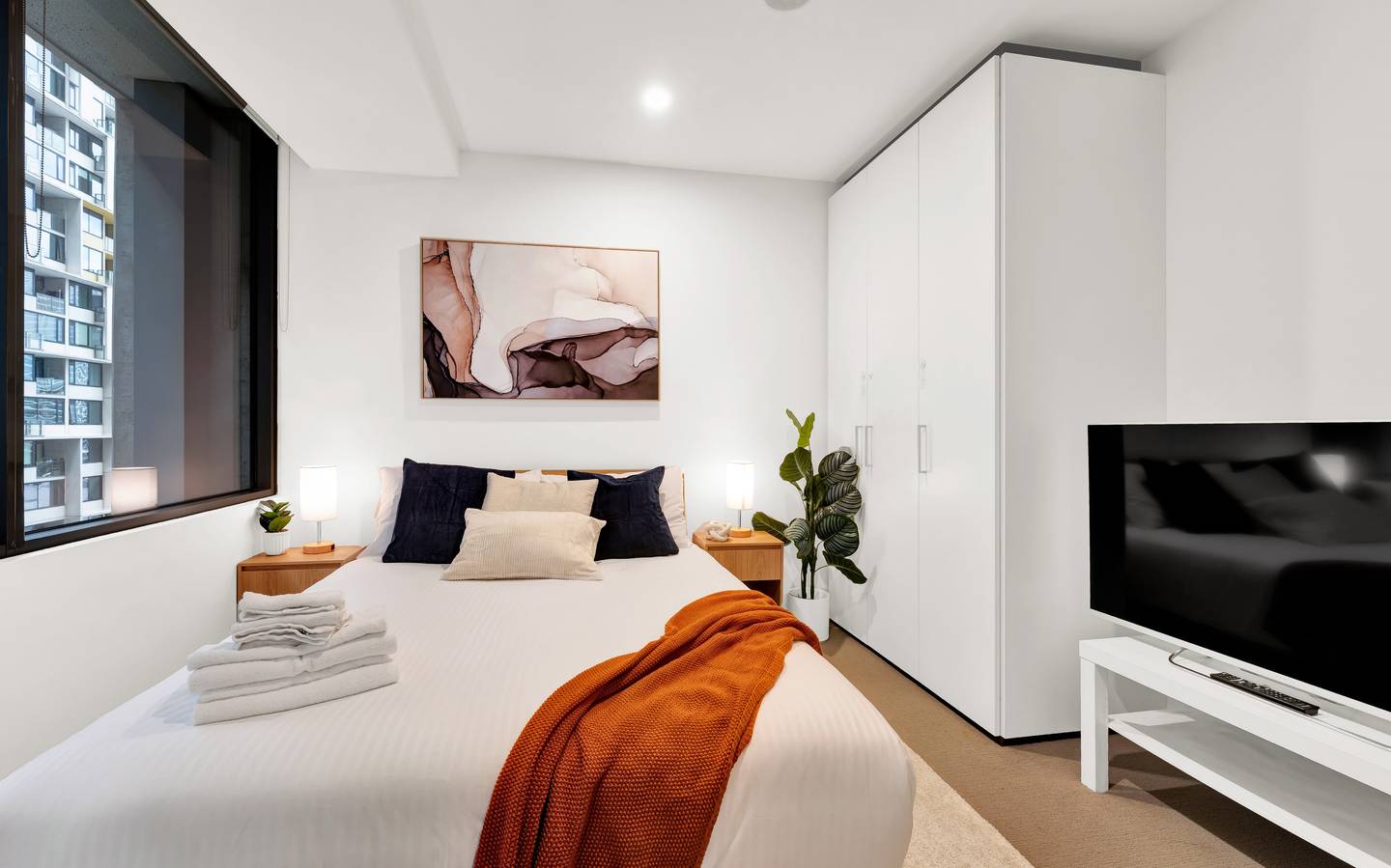 Madison: master bedroom — queen bed dressed in hotel-grade linen, with a blackout blind and its own television
