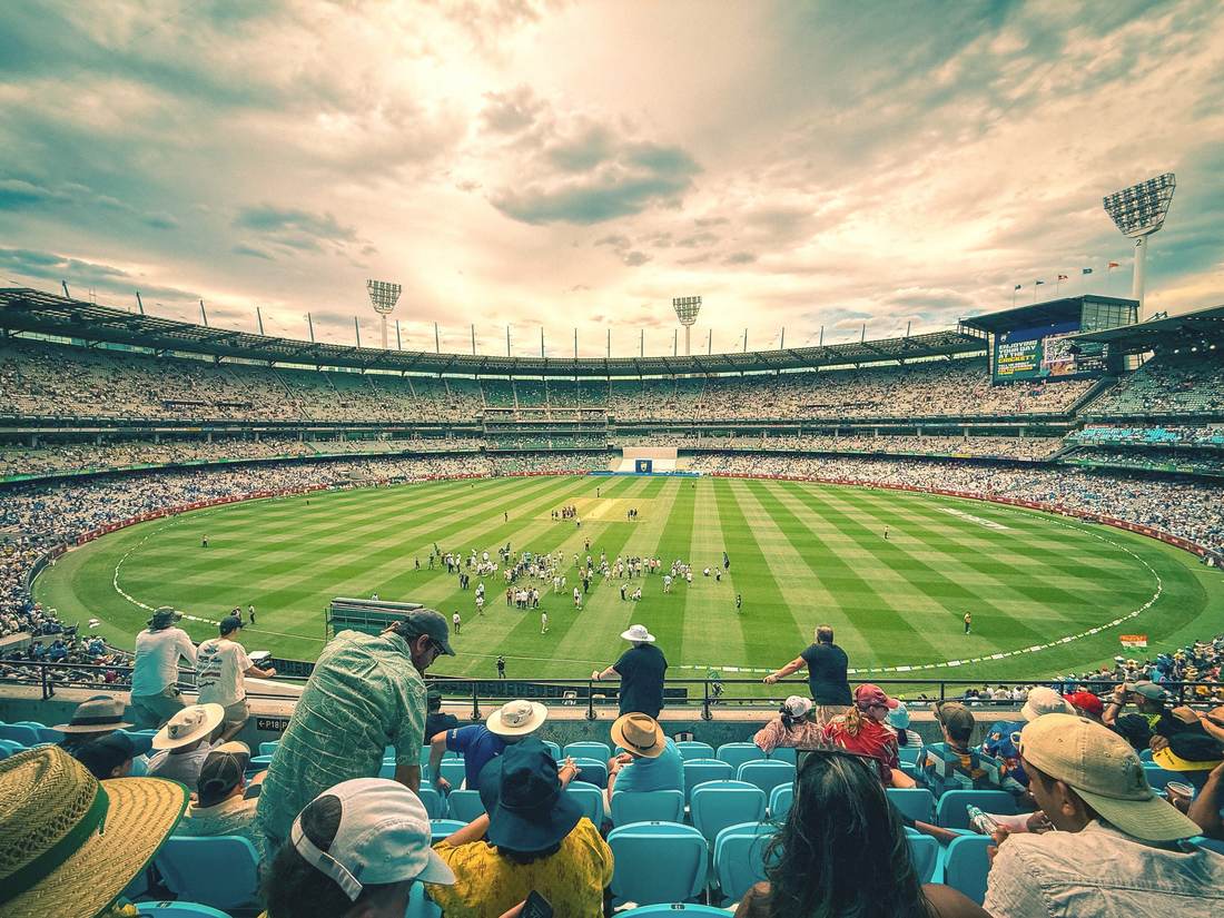 The Melbourne Cricket Ground packed for a cricket match on a bright day, the crowd filling the stands around the oval.