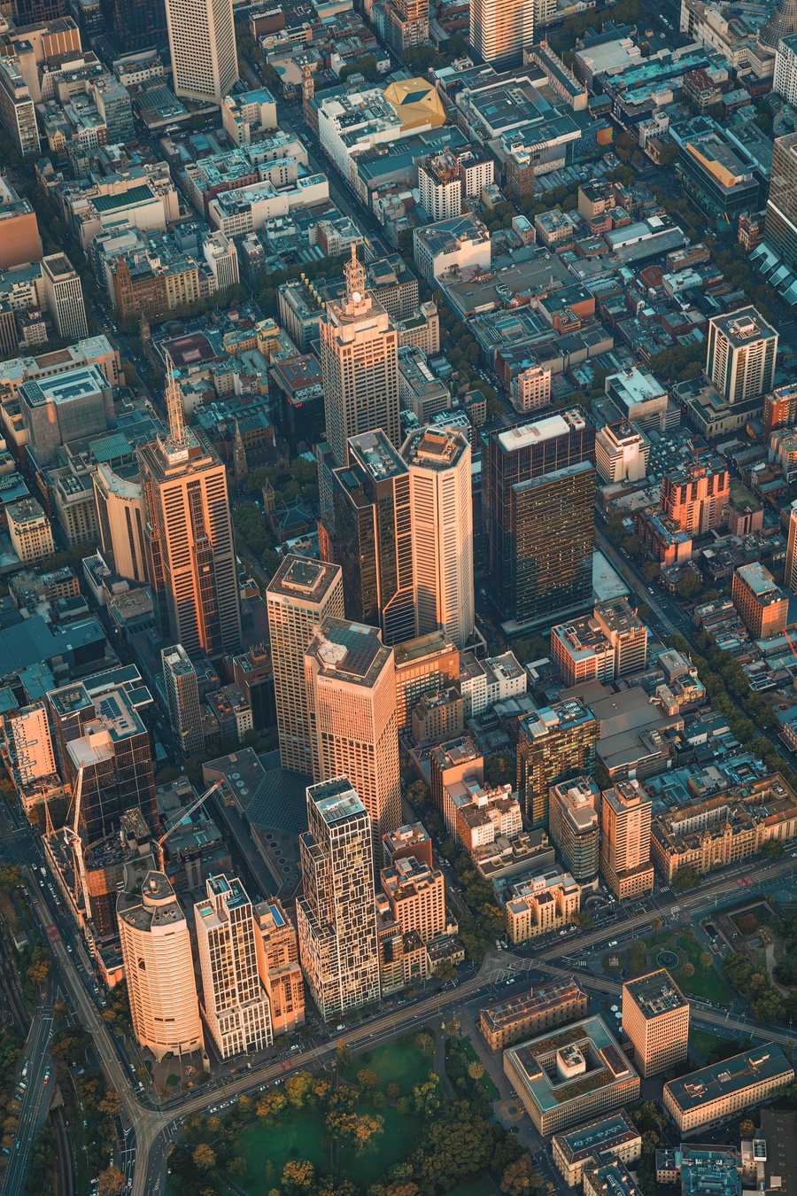Melbourne city centre from above at sunset, its rectangular grid of streets laid out between the towers, with parkland and Parliament along the lower edge.