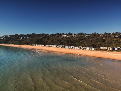 Colourful bathing boxes along a sandy beach at Mornington, the bay clear and calm.