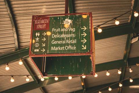 The painted direction sign at Queen Victoria Market under strings of festoon lights.