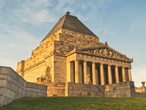 The Shrine of Remembrance glowing in golden evening light under a clear blue sky.