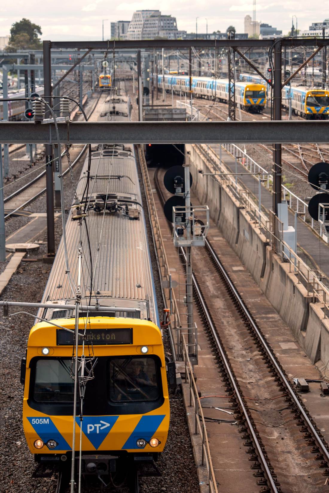 Trains at the platforms of Southern Cross Station in Melbourne on a bright day, the city towers beyond.