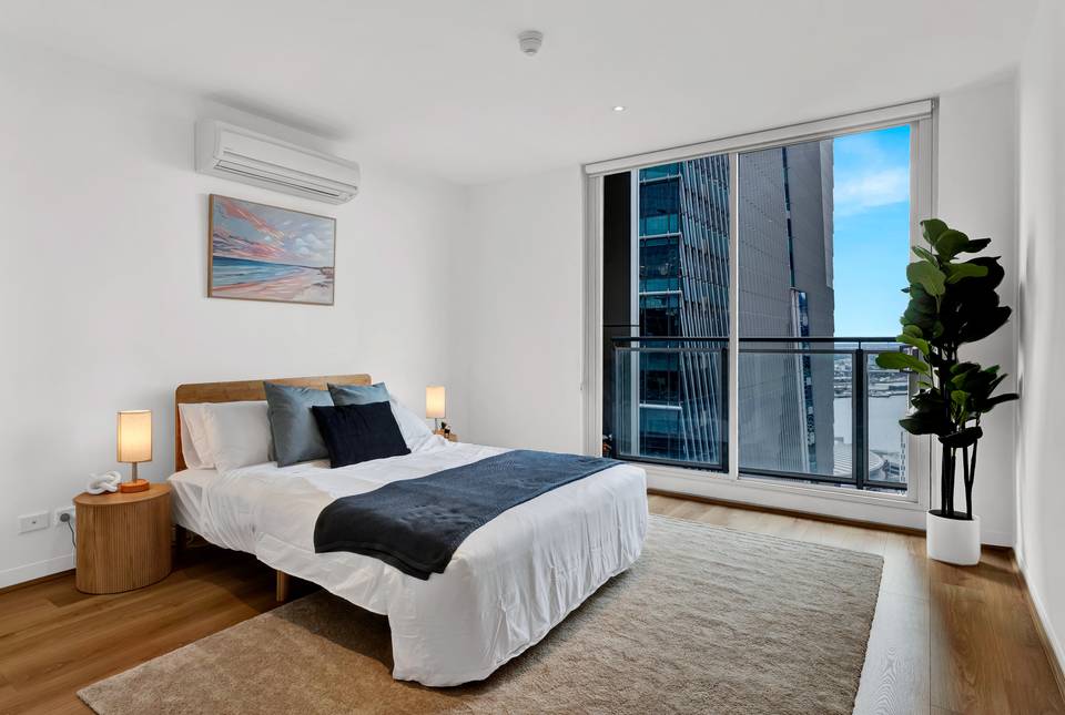 Spencer: master bedroom — queen bed dressed in hotel-grade linen, with floor-to-ceiling glass looking west over Docklands