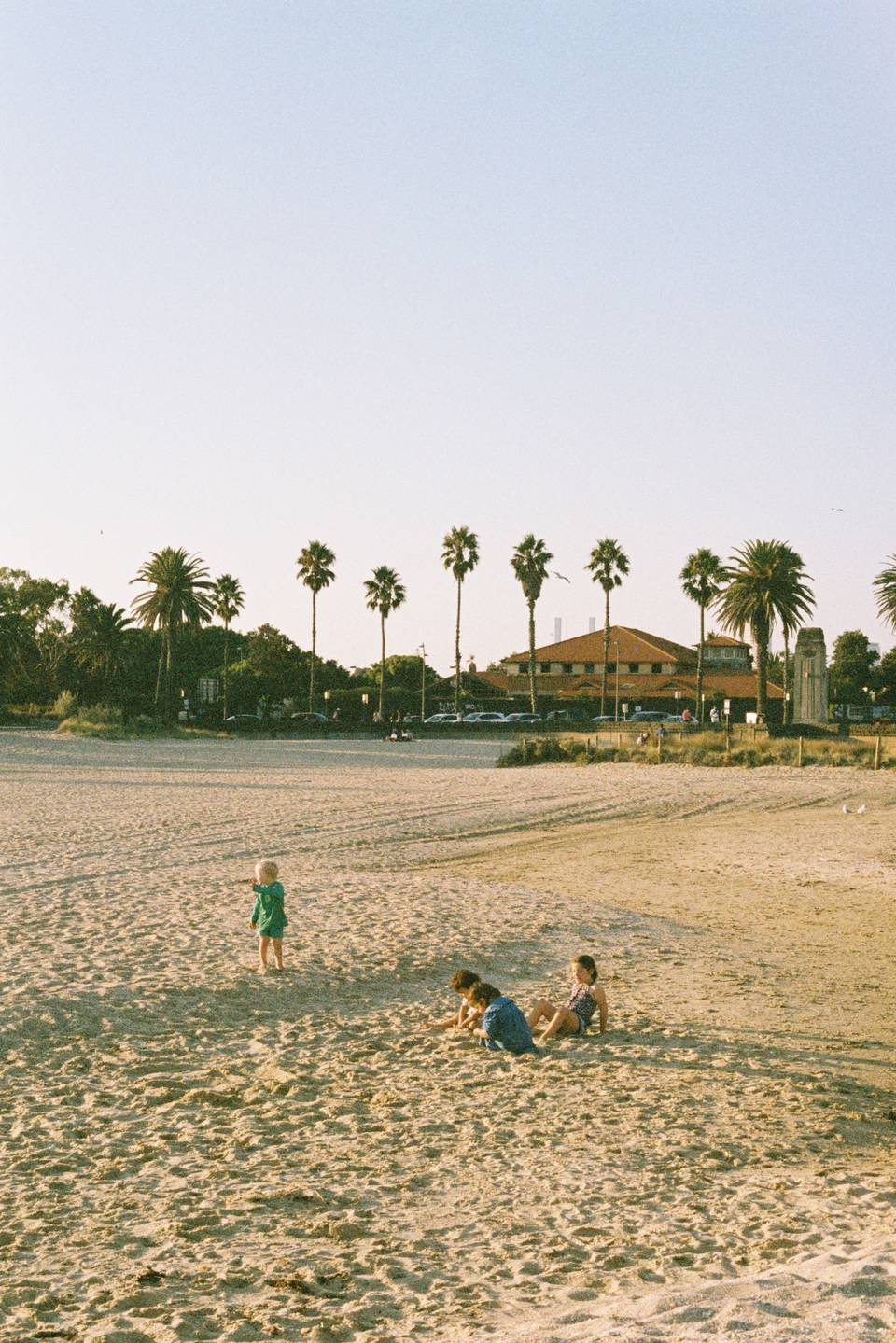 Three children playing on a sandy Melbourne beach on a sunny day.