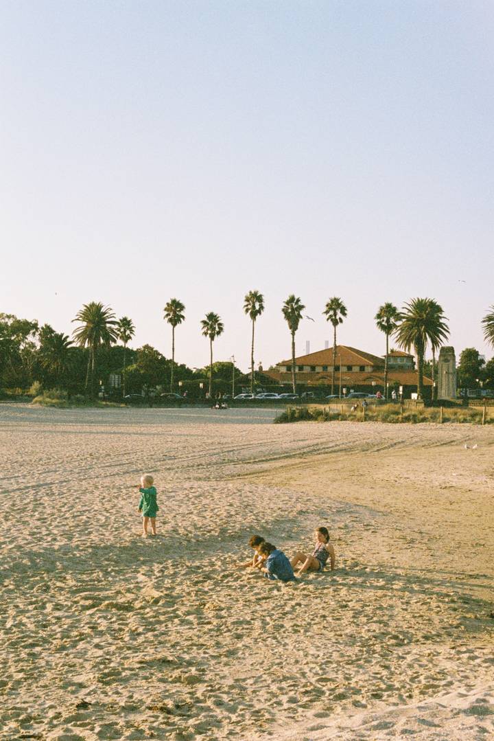 Three children playing on a sandy Melbourne beach on a sunny day.